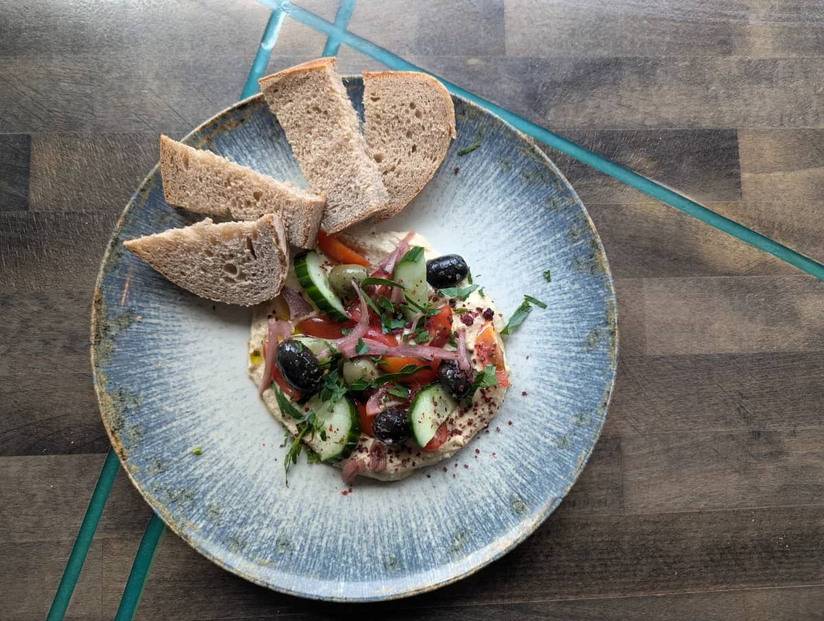 Ein Hauch von Orient — Hummus getoppt mit Tomate, Gurke, roter Zwiebel, Oliven, Kräutern und Sauerteigb bei Kaspio in Stade